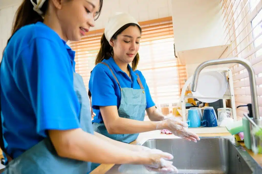 Two women in house cleaners uniforms cleaning around a kitchen sink